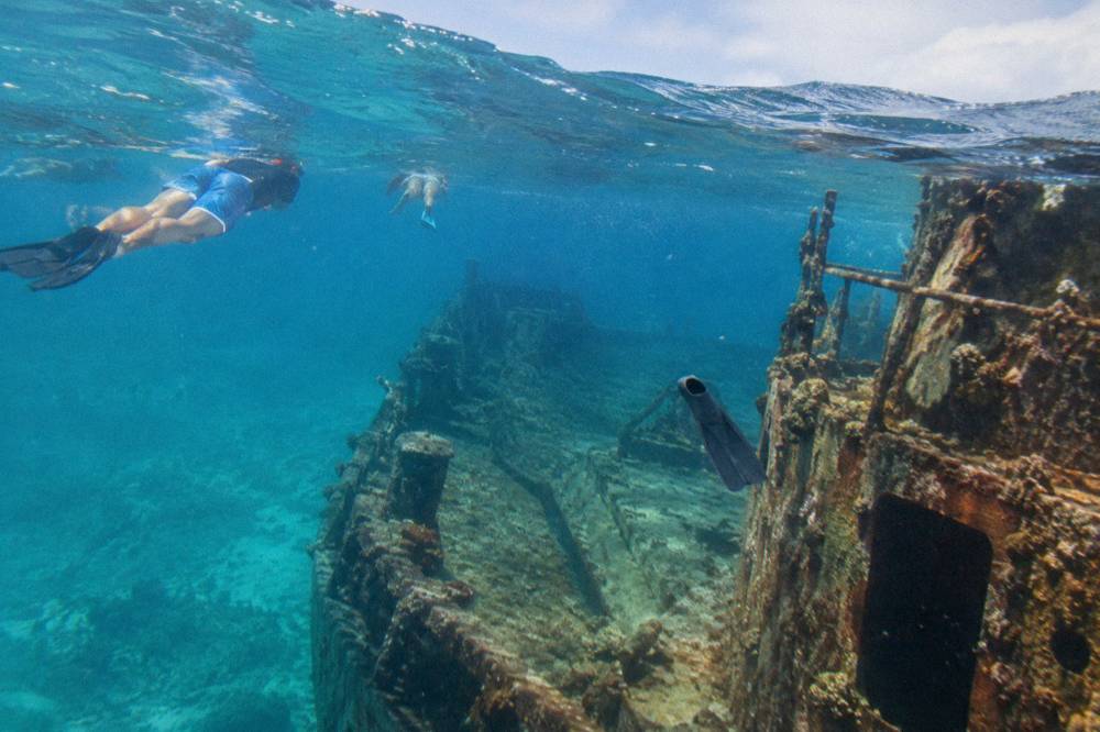 Snorkelers floating above a sunken shipwreck in clear blue water
