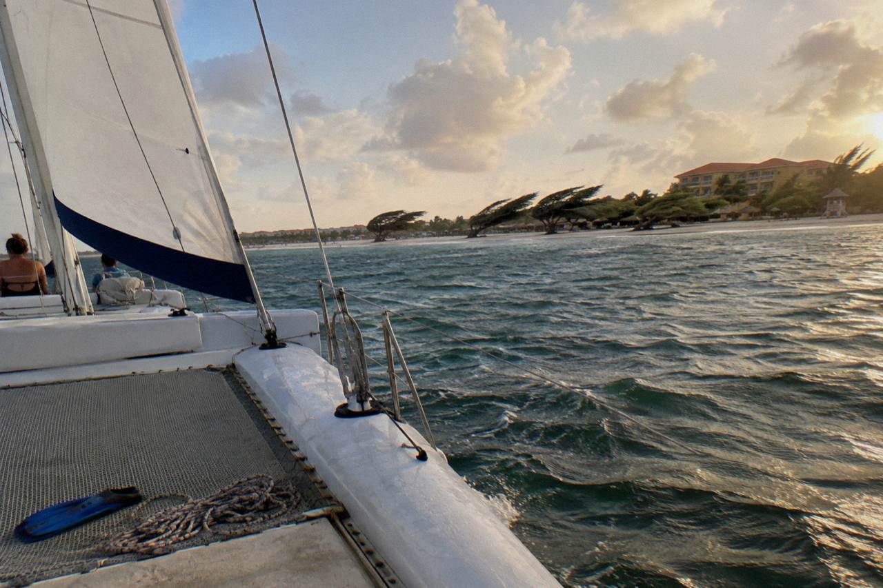 A white catamaran sailing along a calm Caribbean shoreline at golden hour