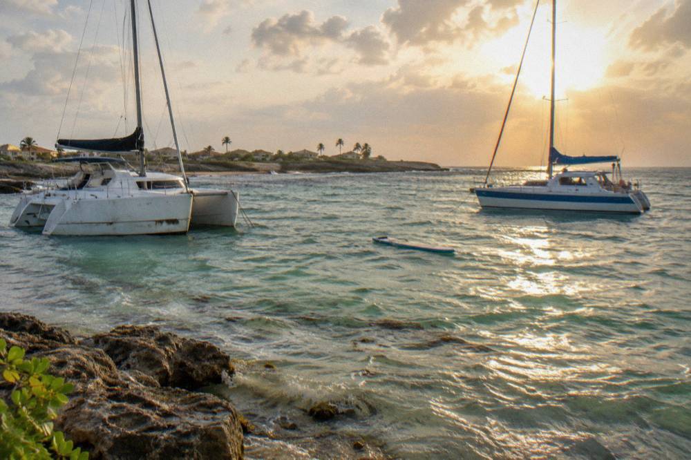 Two catamarans anchored near a beach at golden hour with calm shallow water
