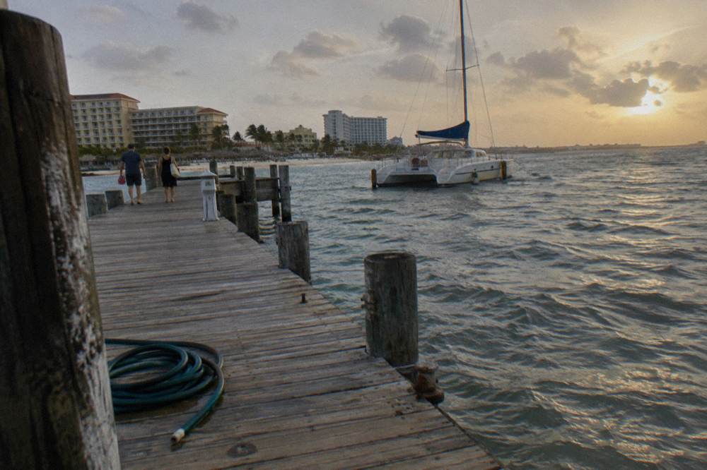 Wooden pier extending into calm evening water with a catamaran moored beyond it