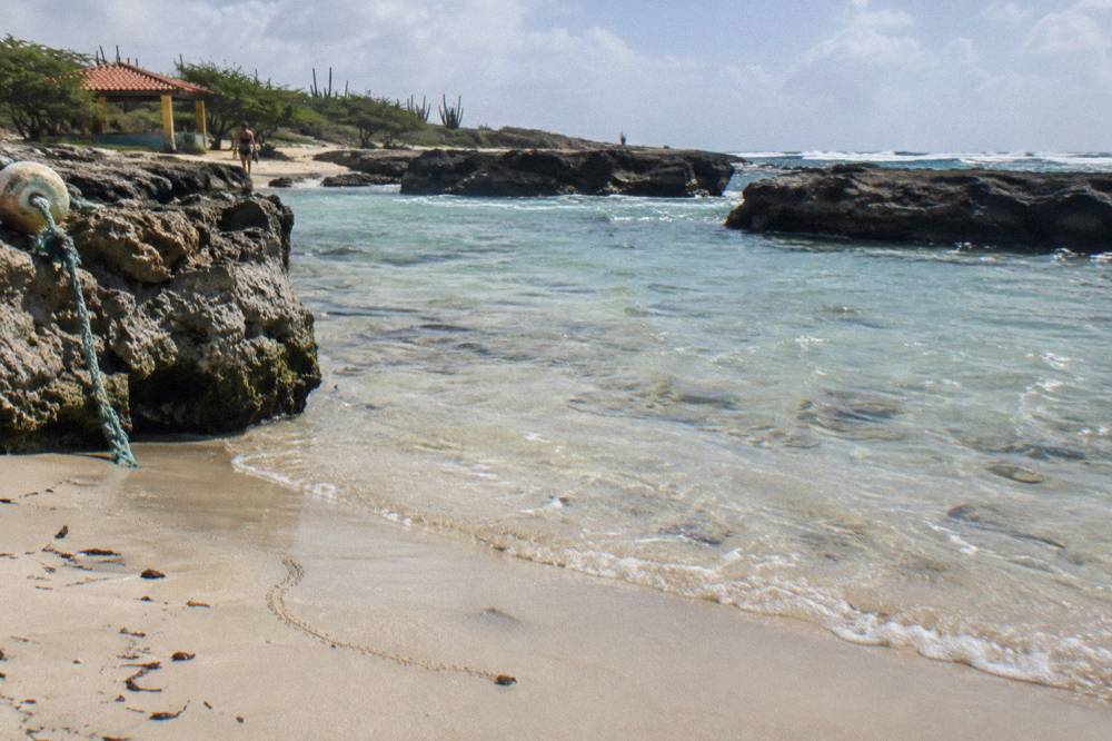 A calm shallow bay with pale sand and clear water sheltered by low rock formations