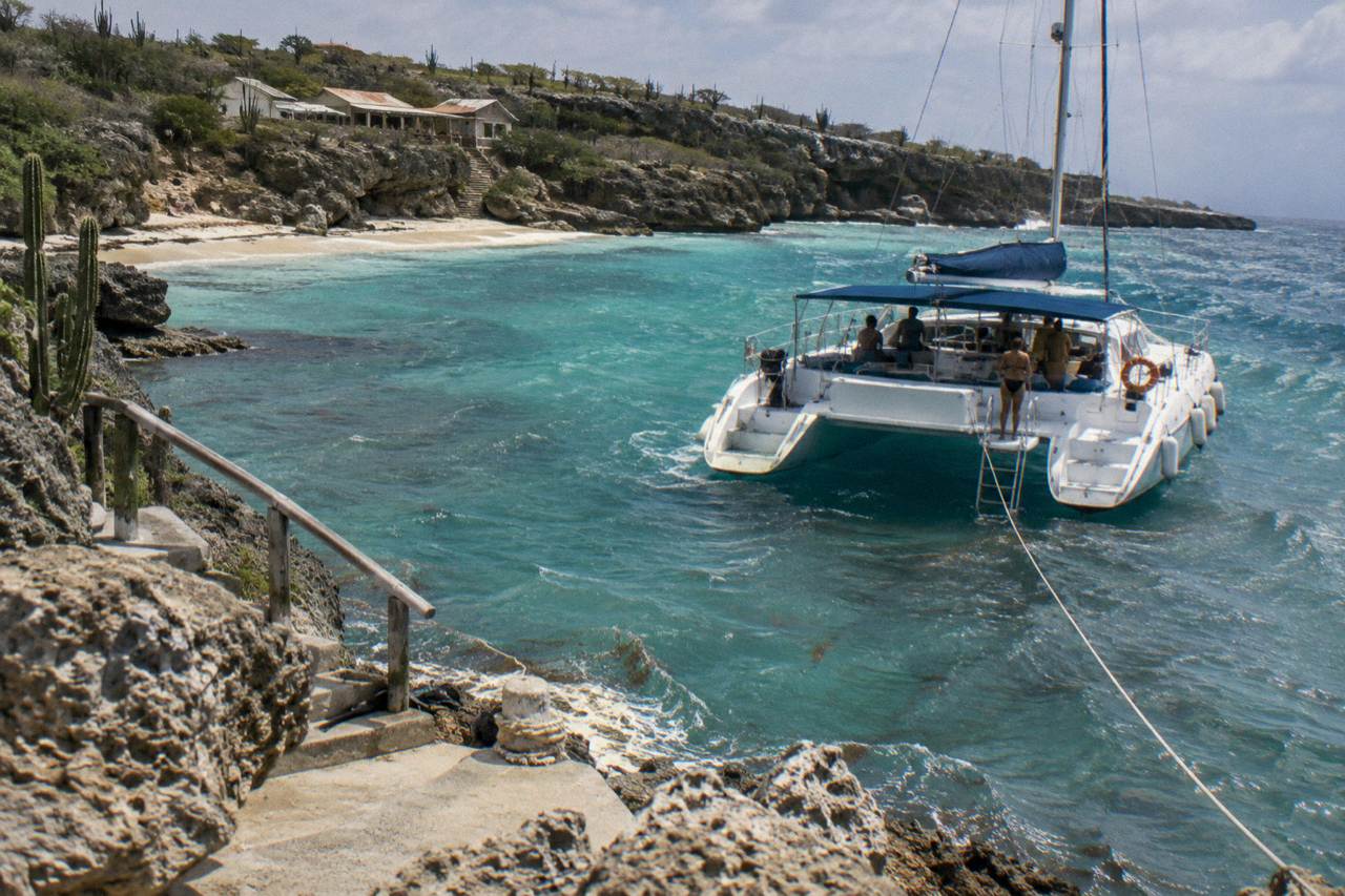 A catamaran anchored in clear turquoise water beside a shallow coral reef in Aruba