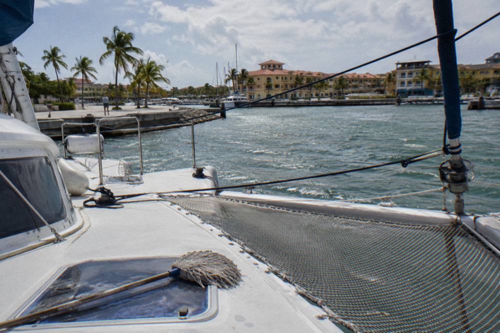 A wide catamaran deck with nets and rigging seen from the bow in bright daylight