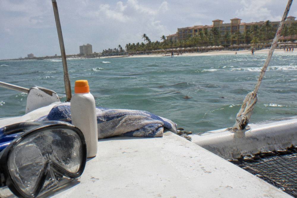 A reef-safe mineral sunscreen bottle resting on a boat deck beside a mask and towel