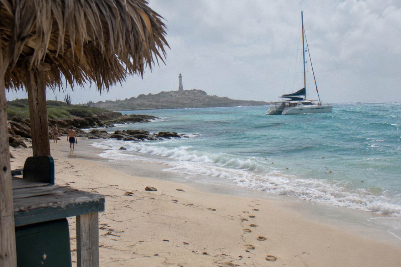 A catamaran at anchor off a calm Caribbean beach with turquoise water along the shoreline