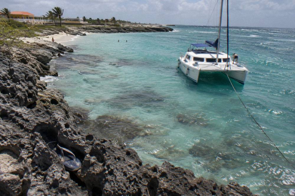 Catamaran moored over pale turquoise water near a rocky shoreline