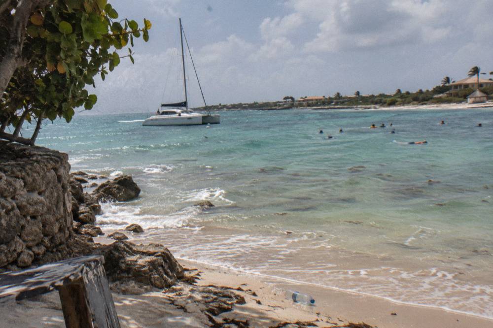 A catamaran moored near a coral reef with snorkelers visible in clear shallow water