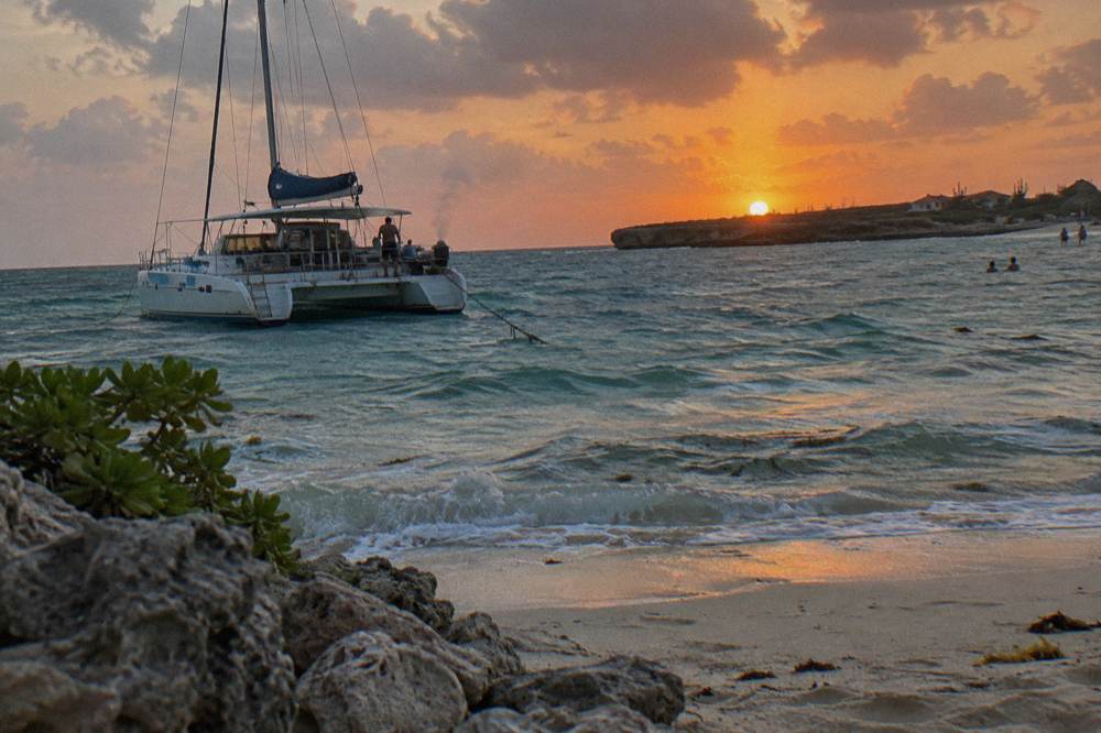 A catamaran at anchor near a beach as the sky turns orange at sunset