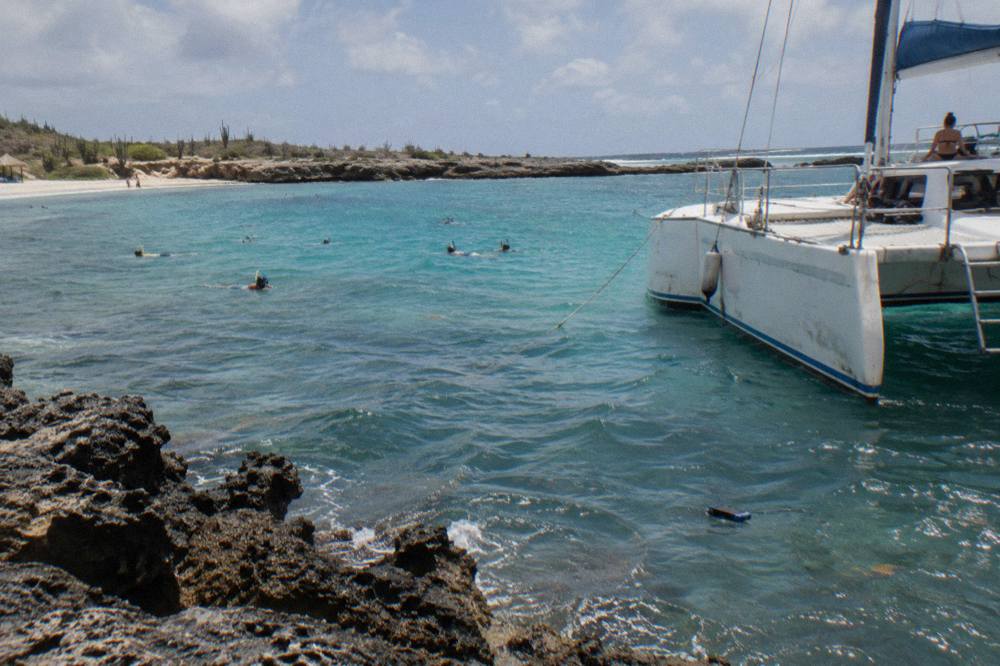A catamaran anchored over pale turquoise water with snorkelers near a reef