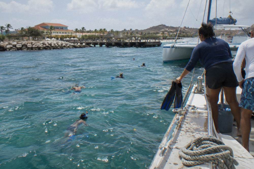 Snorkelers in the water beside a moored catamaran on a sunny afternoon