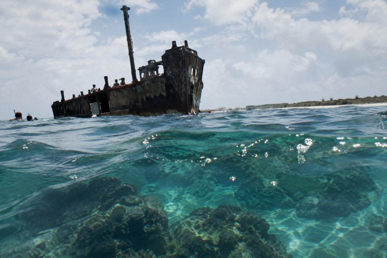 Clear turquoise water over a coral reef with a shipwreck silhouette below the surface