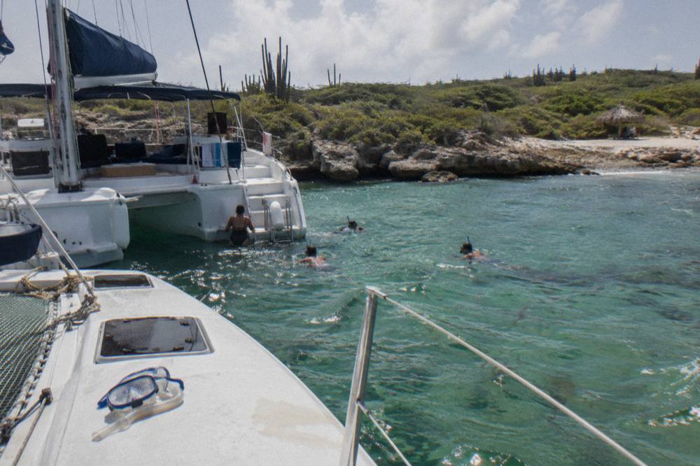 A white catamaran anchored in clear turquoise water with snorkelers near the stern