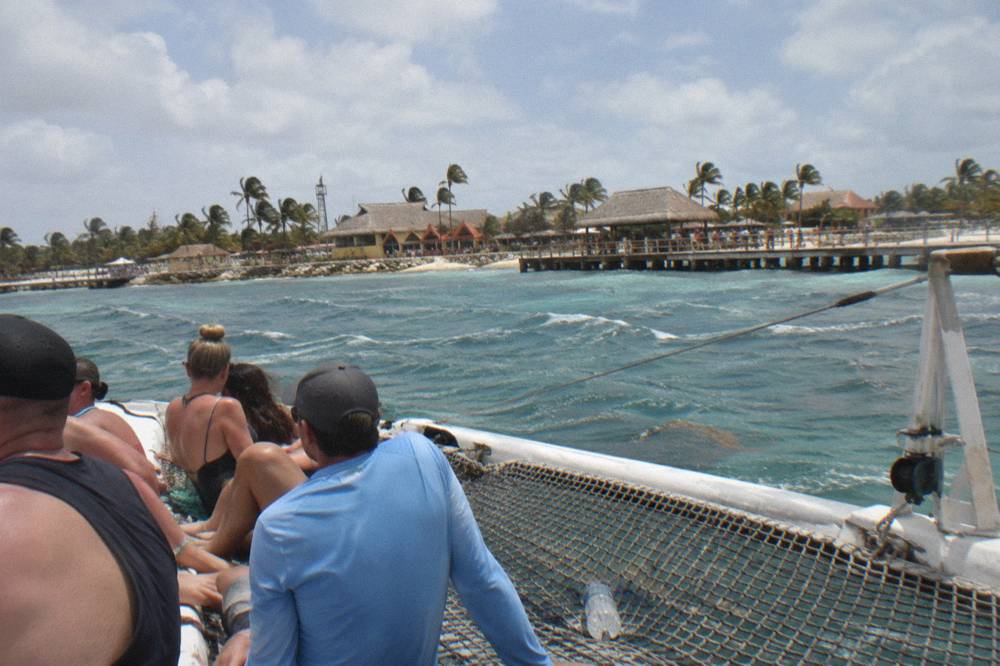 A wide catamaran deck with rows of shaded seating and netting at the bow