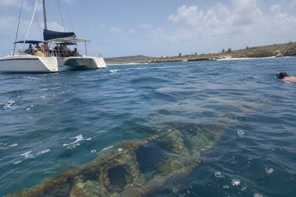 A catamaran anchored near a shipwreck site in clear turquoise water