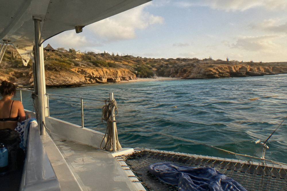 A catamaran deck at golden hour with calm water and a distant shoreline