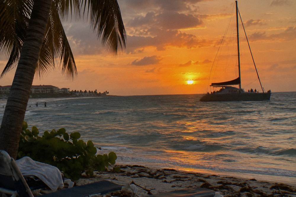 A sailboat silhouette against a bright orange sunset over open water