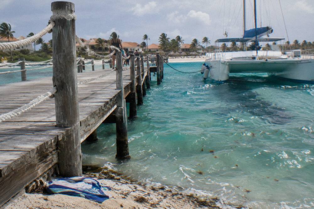 Wooden pier extending from a Palm Beach resort into calm turquoise water with catamarans anchored offshore