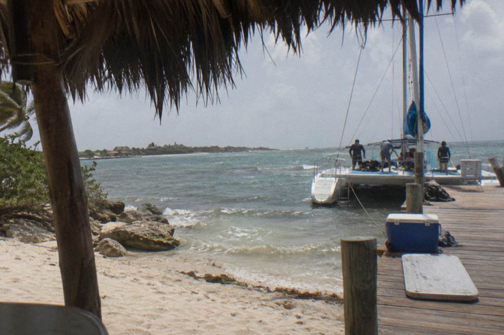 Catamaran moored at a wooden pier with passengers boarding and crew preparing snorkel equipment on deck