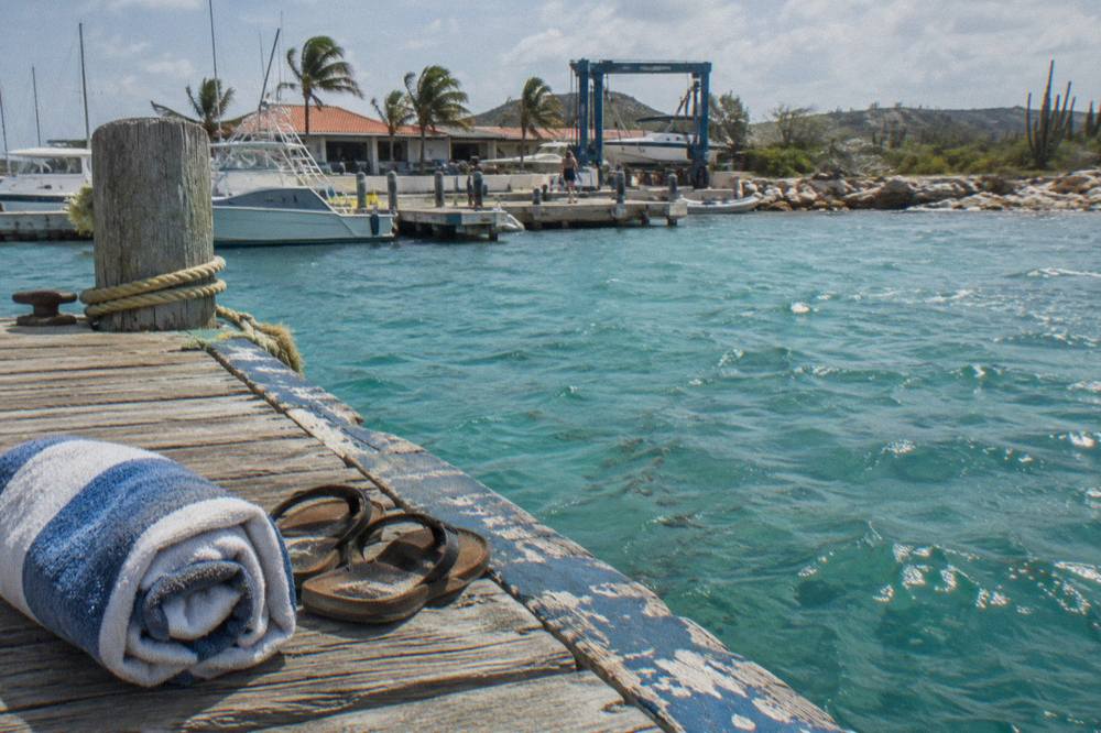 Pair of sandals and a folded towel resting on a wooden boat deck beside turquoise water