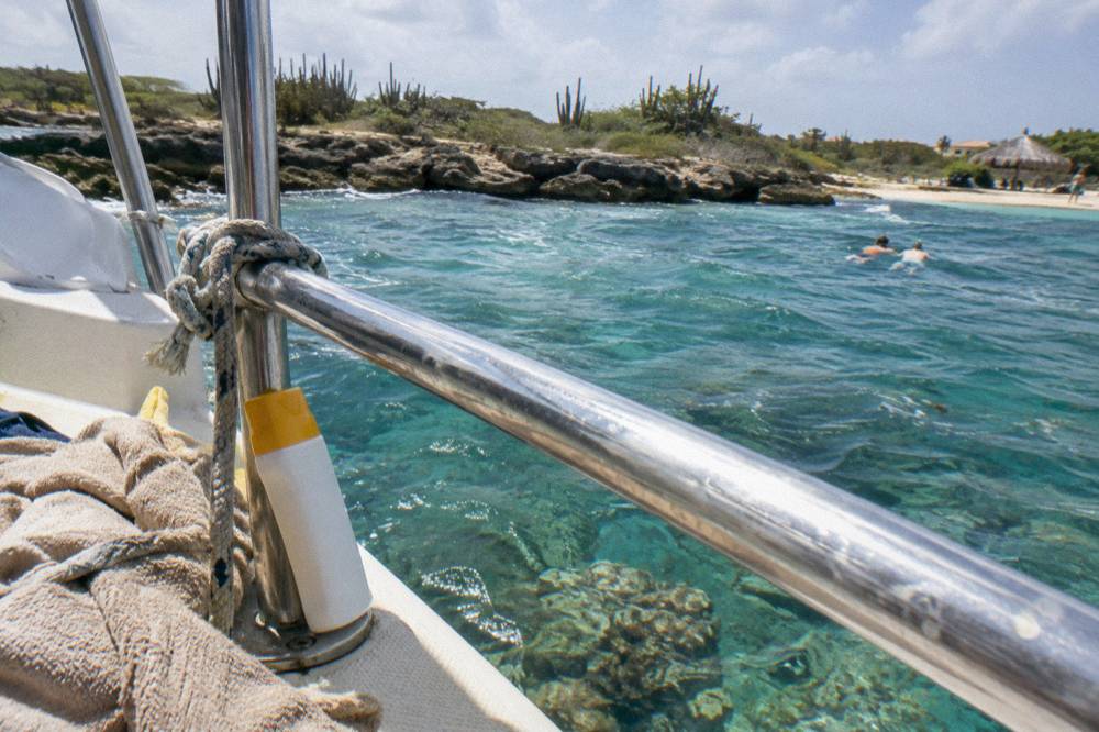 Bottle of mineral sunscreen on a boat rail with clear shallow reef water below