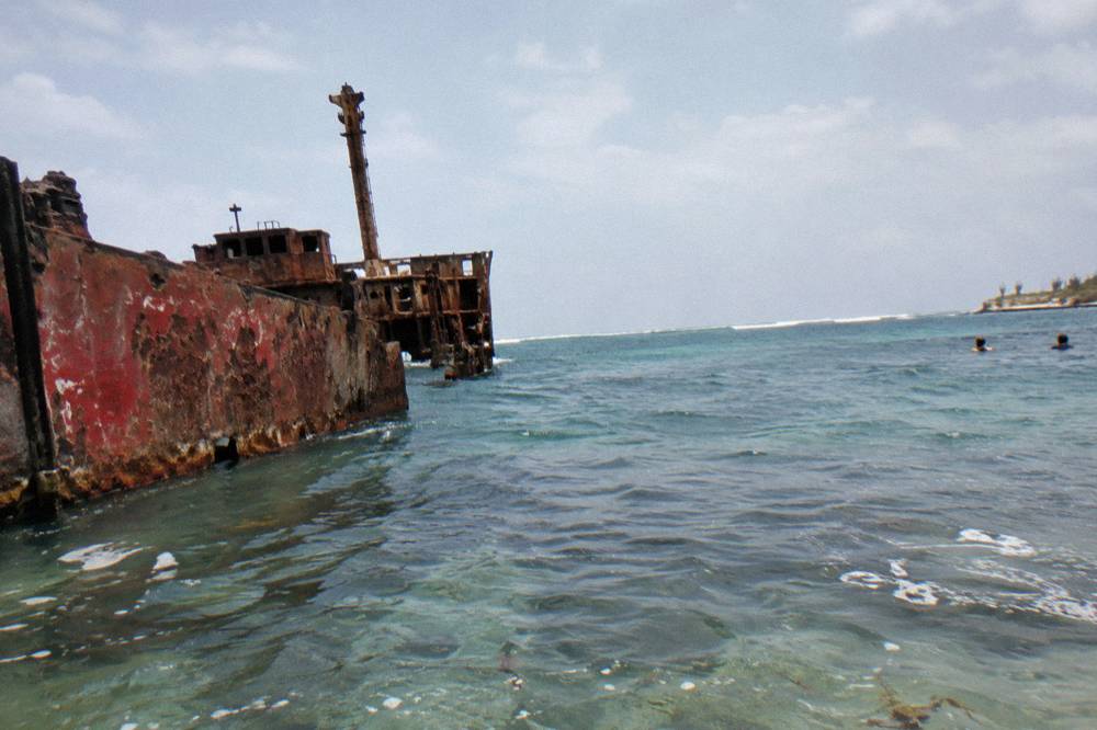 A shipwreck hull breaking the surface of calm sea under a wide sky