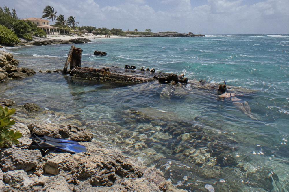 A snorkeler floating over a shallow shipwreck in clear blue water