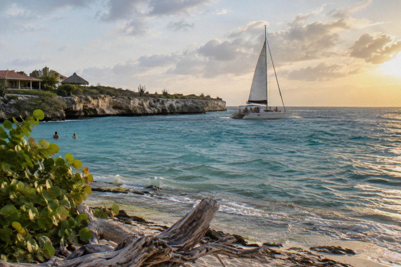 A catamaran sailing along a calm turquoise coastline at golden hour