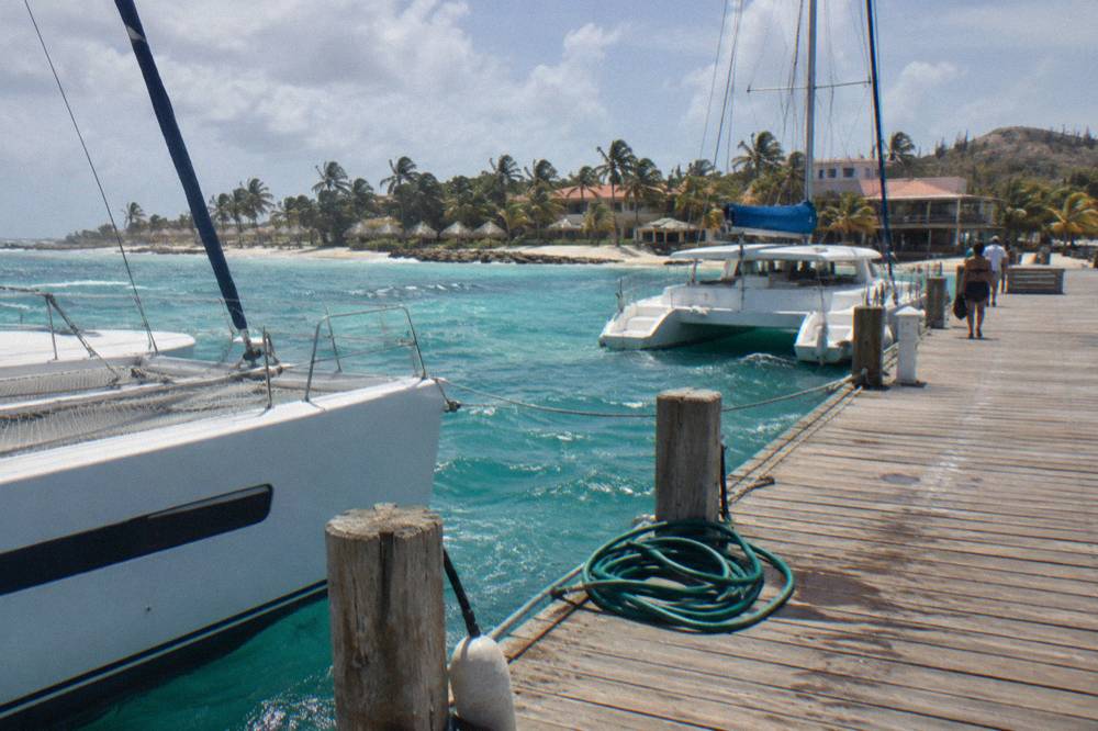 Wooden pier extending over clear turquoise water with catamarans anchored nearby