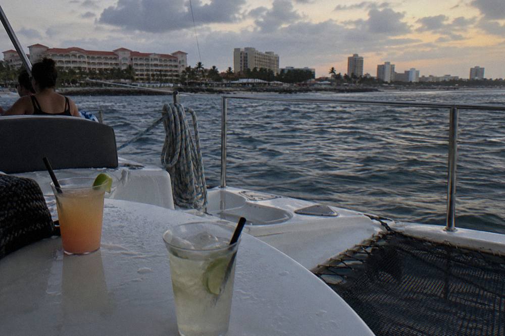 Open deck of a catamaran at dusk with drinks on a table and calm water beyond