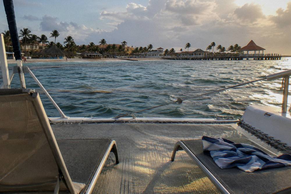 Two lounge seats on a catamaran foredeck facing open water at golden hour
