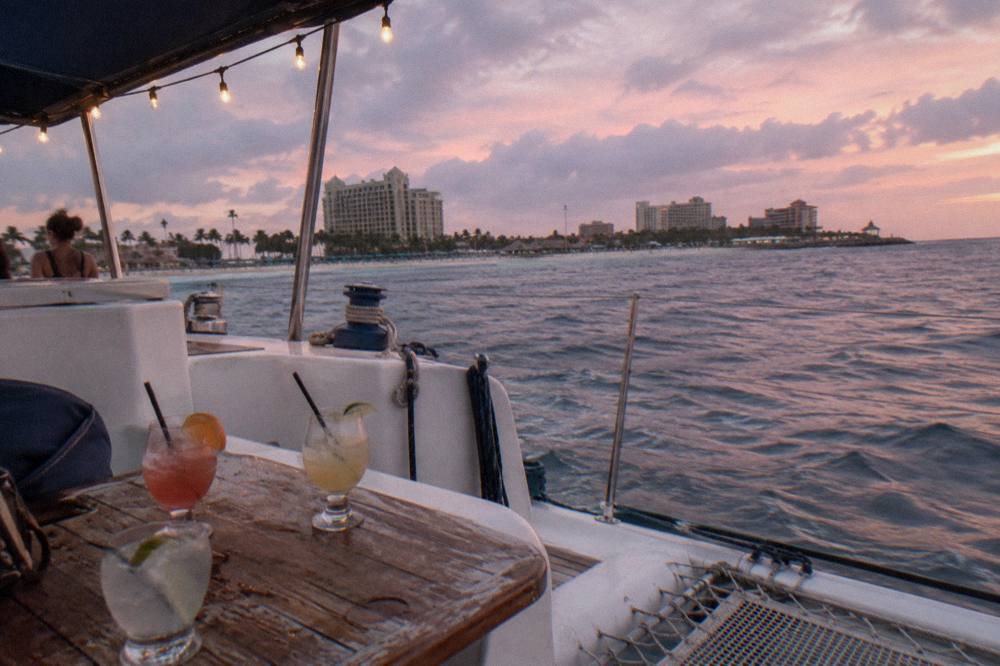 Catamaran deck with string lights and cocktail glasses as the sky turns pink over the sea