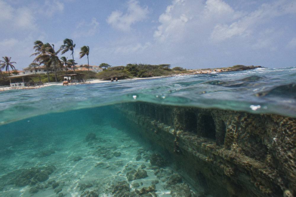 A long sunken ship hull lying on its side in clear blue water with reef fish swimming above it
