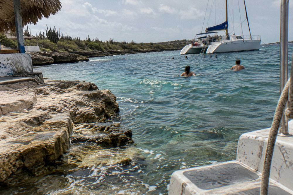 Anchored catamaran with swimmers in clear water near a sandy beach