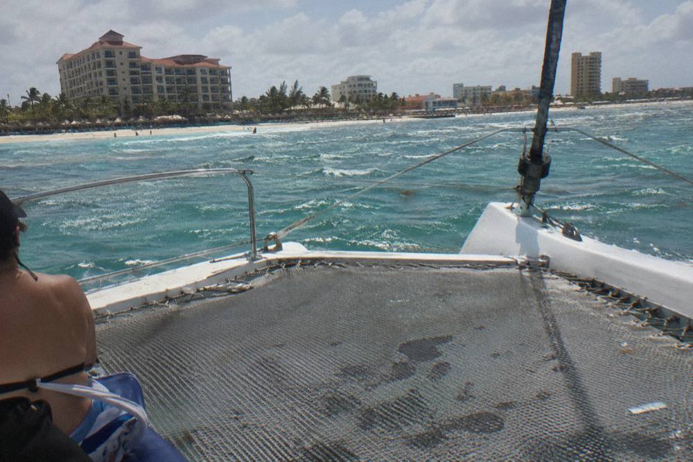 A wide catamaran deck with trampoline nets and calm turquoise water off the bow