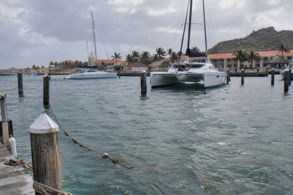 A wooden pier extending over calm turquoise water with catamarans at anchor beyond