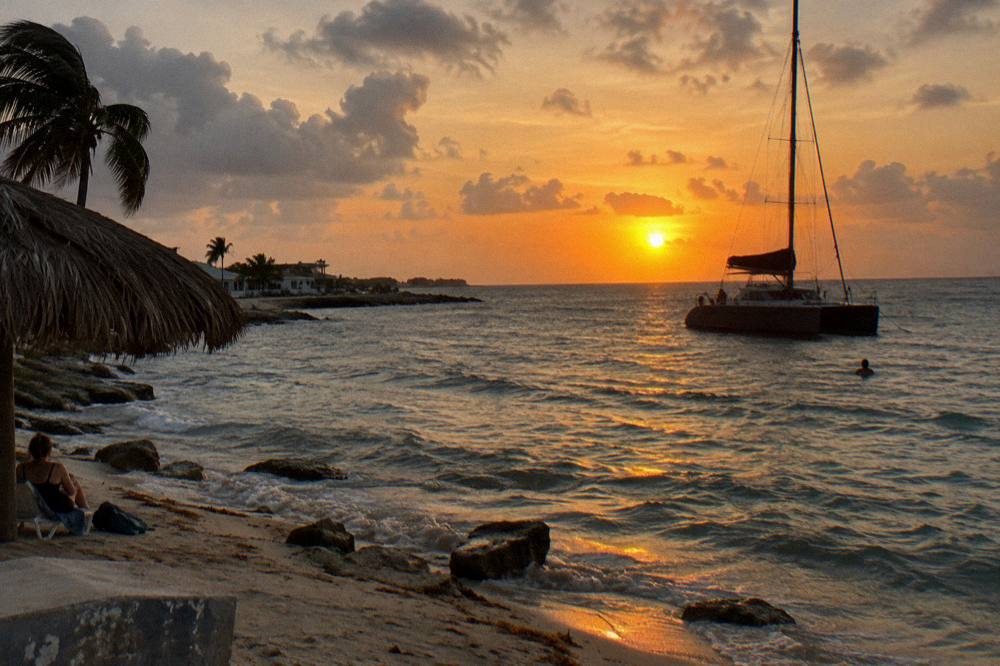 A catamaran silhouette against an orange sunset over calm Caribbean water