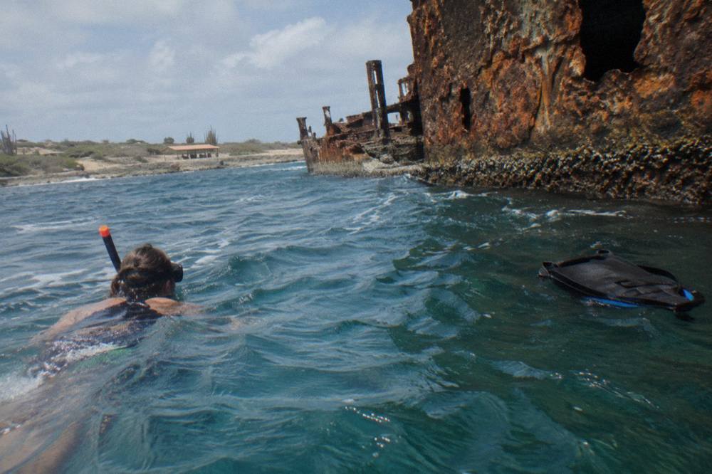 A snorkeler viewing a large shipwreck hull through clear blue water