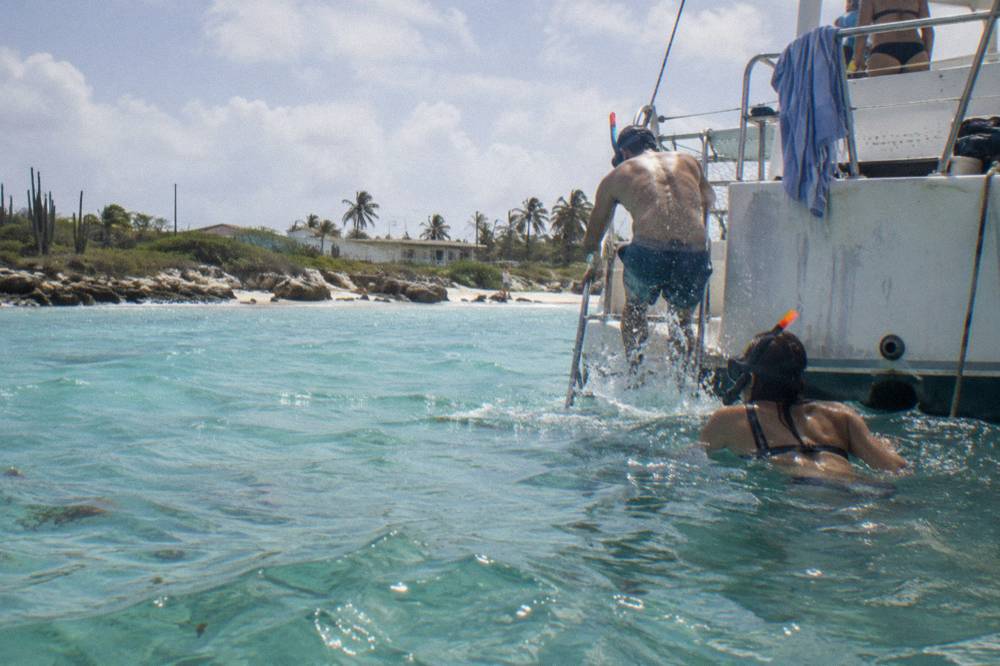 A catamaran moored above turquoise water with snorkelers entering the sea from the stern