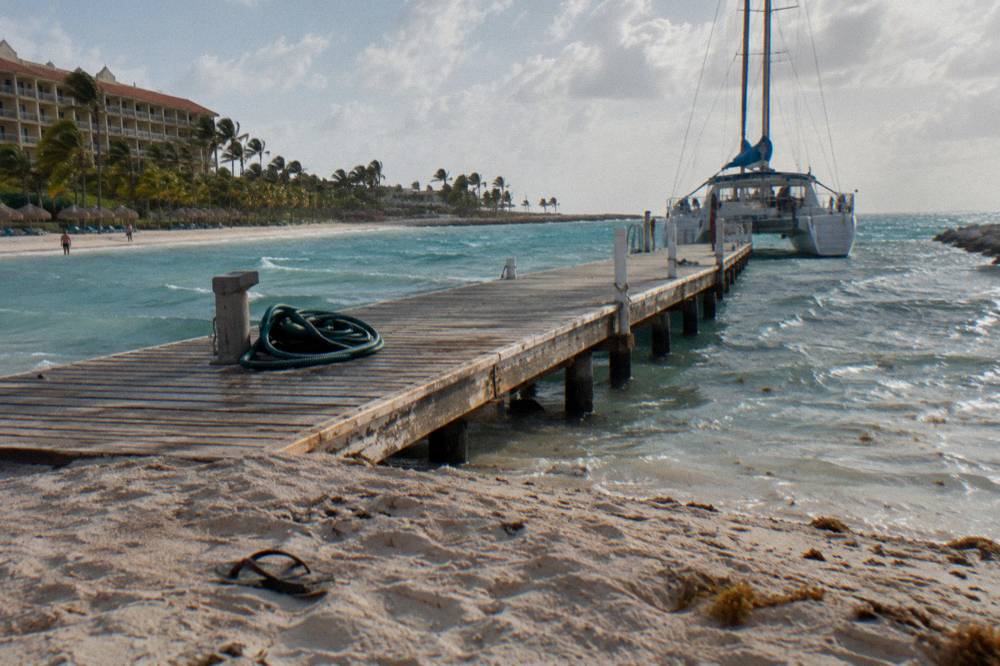 A wooden pier extending into calm turquoise water with a catamaran at anchor beyond
