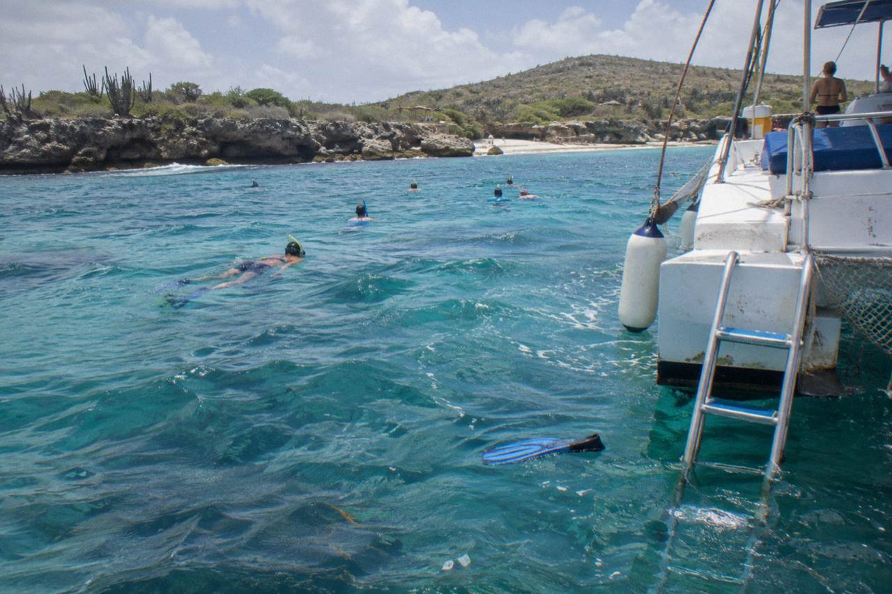 Snorkelers floating above a coral reef in clear turquoise water beside an anchored catamaran