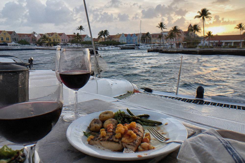 A plated dinner served on a catamaran deck table at sunset with glasses of wine