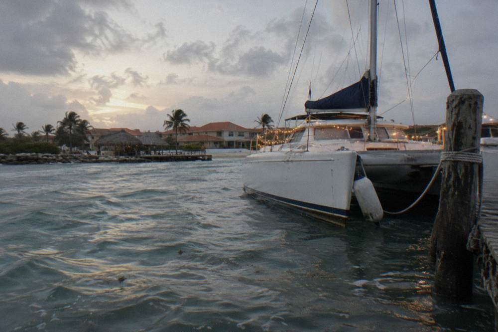 A catamaran moored at a wooden pier at dusk with string lights and calm water