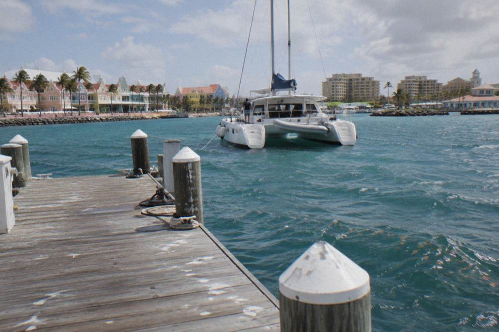 A catamaran moored at a wooden pier with calm blue water and distant hotel towers along the shore