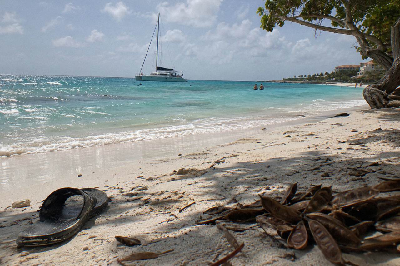 Clear turquoise water along a sandy Aruba beach with a catamaran anchored offshore under an afternoon sky