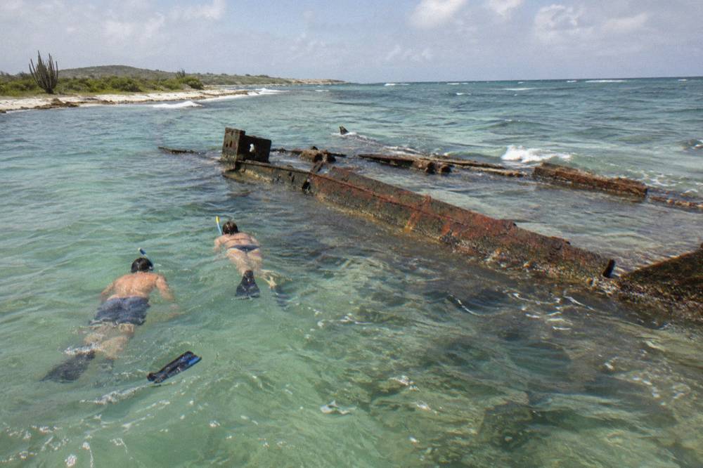 Snorkelers floating above a sunken shipwreck in turquoise water
