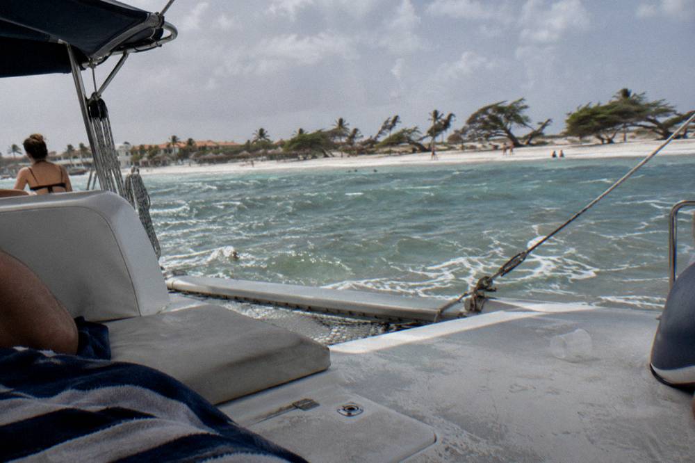 A catamaran deck with cushions and shade at anchor near a beach