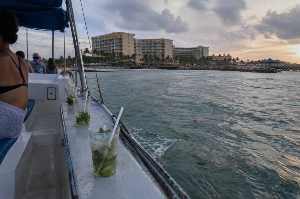 Open deck of a catamaran at dusk with drinks glasses lined along the rail and calm sea beyond