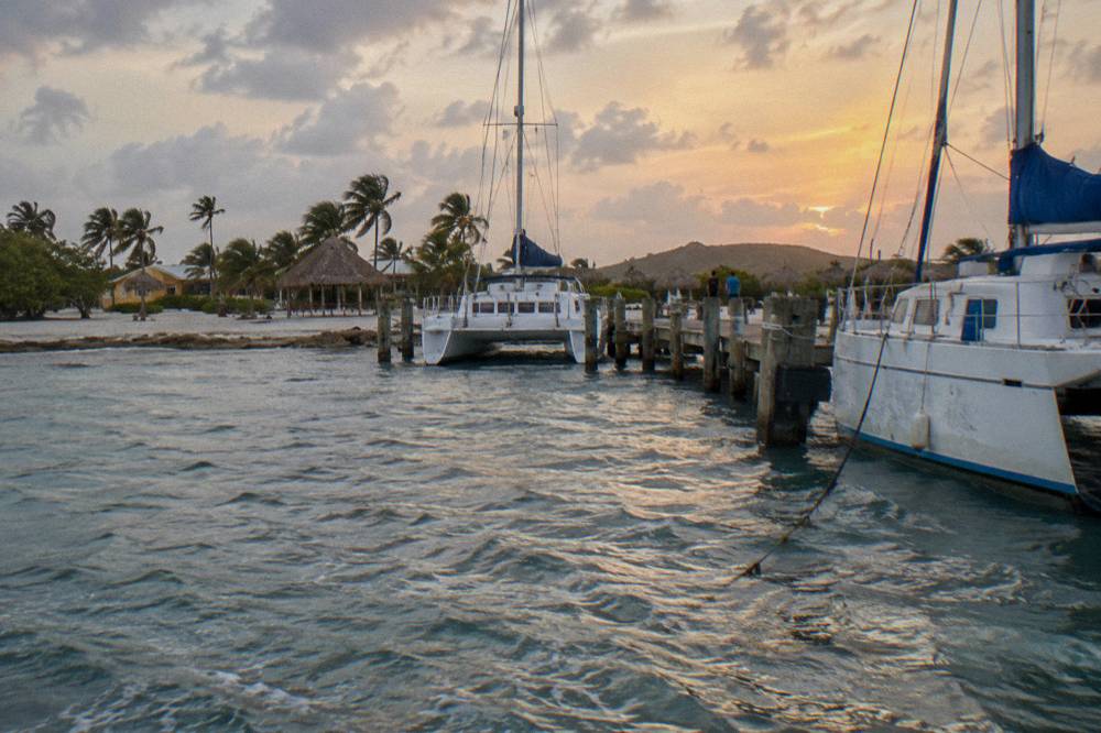 Wooden pier extending into calm blue water with catamarans moored nearby at dusk