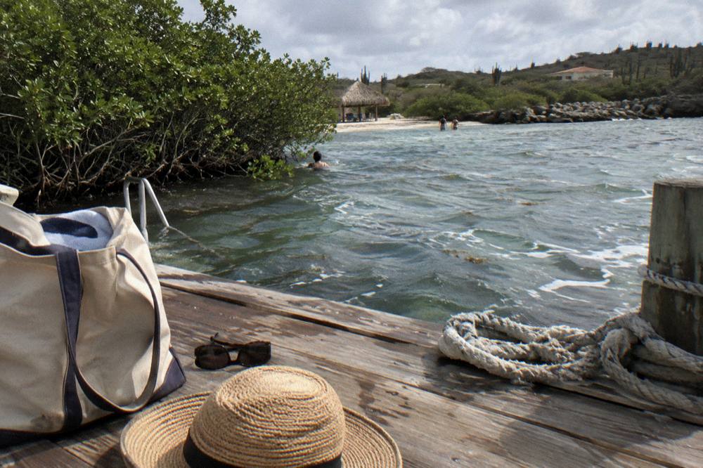 Beach bag, sunglasses and a sun hat resting on a wooden dock beside mooring lines