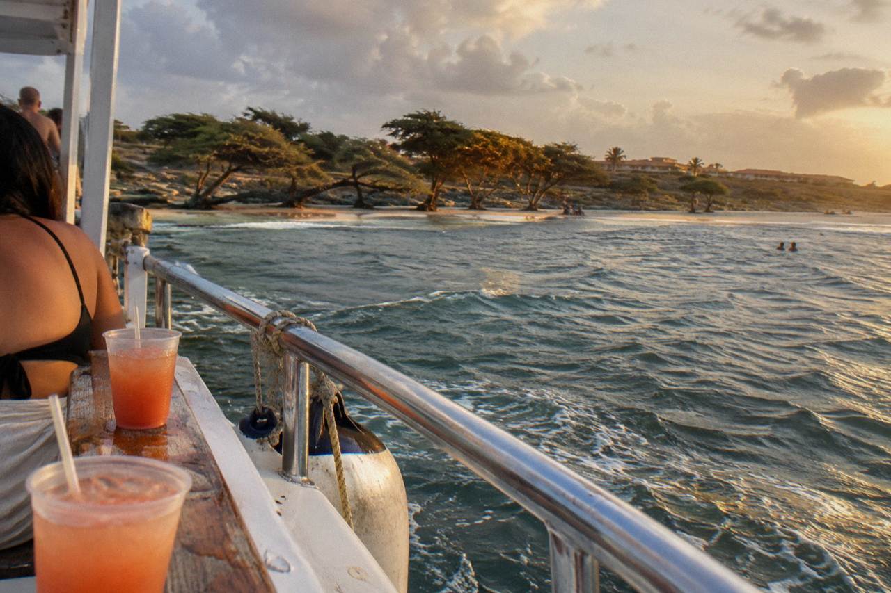 Catamaran sails along a calm tropical coastline at golden hour with drinks on the deck rail